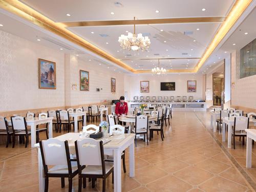 Zhangjiang维也纳国际酒店 (湖南常德桃源龙八店)的一间设有白色桌椅的餐厅,中间有一个人站着
