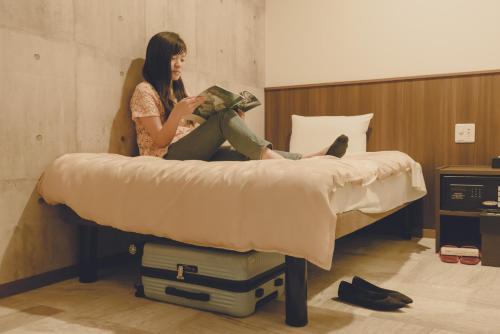 那霸Grand Cabin Hotel Naha Oroku for Men / Vacation STAY 62323的坐在床上读书的女人
