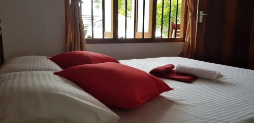 韦利格默One More Day Hostel的一张带红色和白色枕头的床和窗户