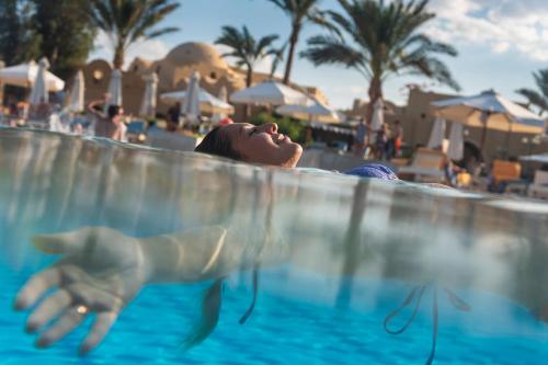 赫尔格达Three Corners Rihana Resort El Gouna的女人在游泳池里看着海豚