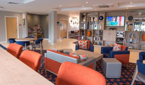 邓弗姆林快捷假日丹弗姆林酒店的一间配备有橙色和蓝色椅子及桌子的等候室