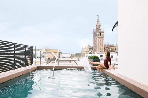 塞维利亚Joya del Casco Boutique Hotel by Shiadu的坐在带游泳池的建筑物屋顶上的女人