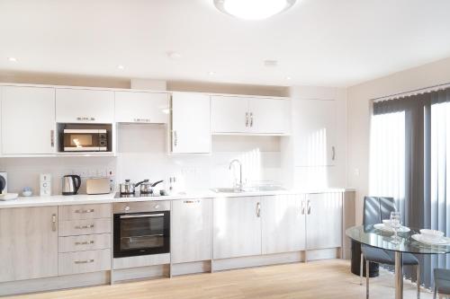 剑桥Citystay - Hinton House的厨房配有白色橱柜和玻璃桌