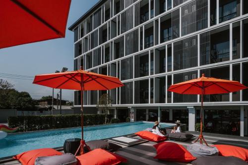 曼谷The Iconic Hotel Don Mueang Airport的一组椅子和遮阳伞,位于游泳池旁