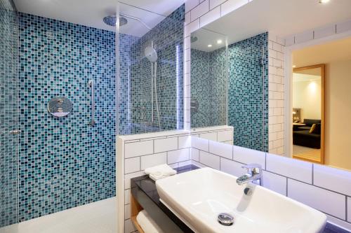 希灵登Holiday Inn London Heathrow - Bath Road, an IHG Hotel的浴室设有水槽和蓝色瓷砖淋浴。