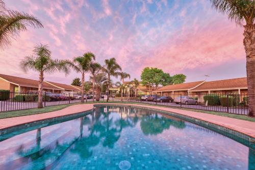 墨尔本Best Western Melbourne Airport的棕榈树和日落的游泳池