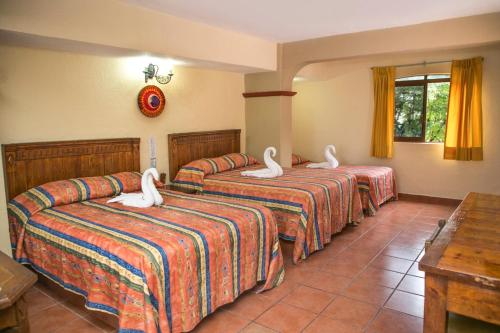 阿卡普尔科Hotel Hacienda María Eugenia的酒店客房设有三张床,上面有天鹅