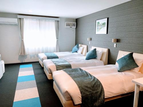 轻井泽Sora Hotel Karuizawa Outlet的酒店客房设有三张床和窗户。