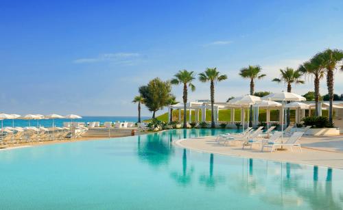 梵蒂冈角Capovaticano Resort Thalasso Spa的一个带椅子和遮阳伞的游泳池以及大海