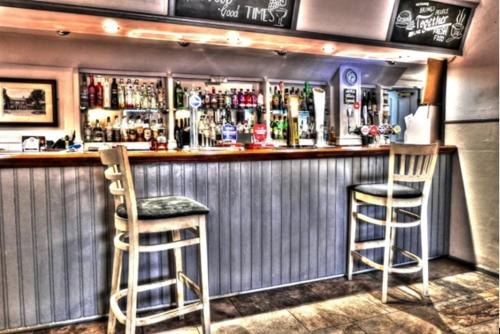 SharnbrookThe Fordham Inn的酒吧设有两把椅子和一个带饮料的吧台