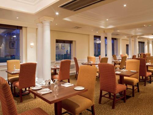 温彻斯特温彻斯特韦塞克斯美居酒店的餐厅设有木桌、椅子和窗户。