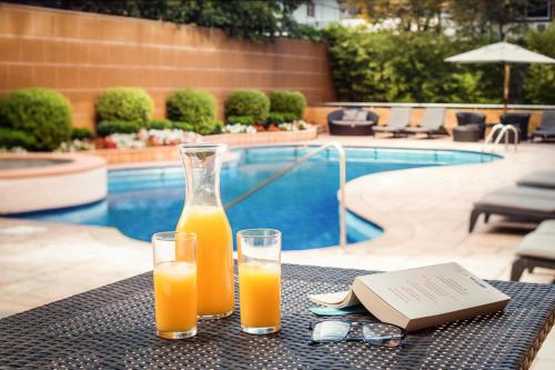 圣地亚哥Boulevard Suites Ferrat的两杯橙汁放在桌旁的游泳池边