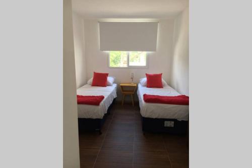 科洛尼亚-德尔萨克拉门托Apto céntrico con wifi的客房设有两张带红色枕头的床和窗户。