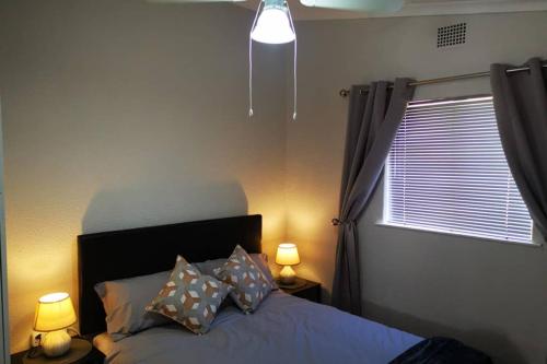 开普敦The Smiths Self Catering Cottage的一间卧室配有一张带两盏灯的床和一扇窗户。