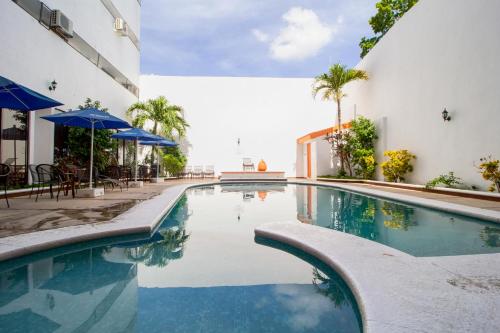 梅里达梅里达大使酒店的一座带蓝色遮阳伞的游泳池,位于一座建筑旁边