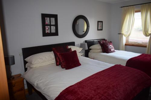 阿维莫尔Dunroamin Self-Catering Apartment的一间卧室配有两张带红色枕头和镜子的床