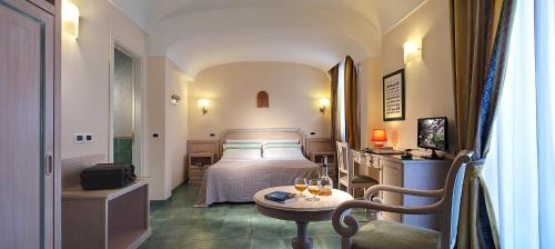 伊斯基亚皇家温泉酒店的一间卧室配有一张床和一张桌子及一杯葡萄酒