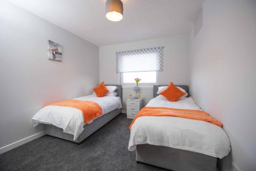 威萧PREMIER - Wishaw En-Suite Apartment的卧室内的两张床,配有白色的墙壁和橙色的枕头