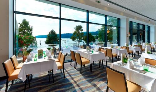 沃尔特湖畔佩莎赫Parkhotel Pörtschach - Das Hotelresort mit Insellage am Wörthersee的餐厅设有白色的桌椅和大窗户。