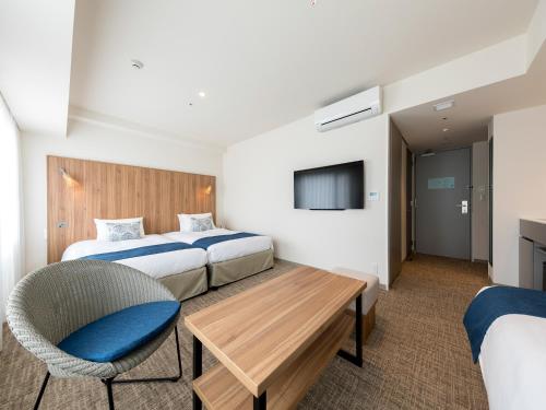 那霸Tokyu Stay Okinawa Naha的酒店客房,配有两张床、一张桌子和一把椅子