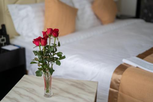 仰光Hotel Sanchaung的一张桌子上的一个红玫瑰花瓶,床边