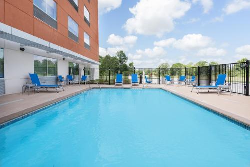 布赖恩Holiday Inn Express & Suites Bryan - College Station, an IHG Hotel的一座带蓝色椅子的游泳池,位于大楼旁