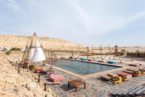 达赫拉Les Dunes de Dakhla的沙漠中的游泳池,带椅子和帆船