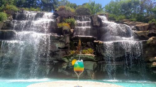 圣洛伦索法泽达维斯塔阿莱格里酒店的瀑布在游泳池里,在瀑布前喝一杯