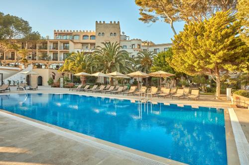 帕格拉Secrets Mallorca Villamil Resort & Spa - Adults Only (+18)的大楼前的带椅子和遮阳伞的游泳池