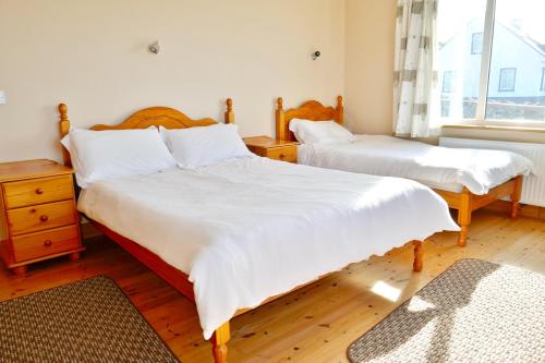 杜林Cois Farraige的一间卧室设有两张带白色床单的床和窗户。