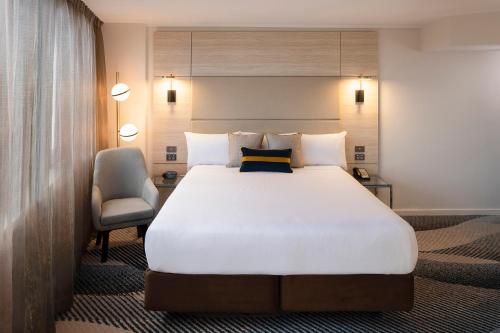 悉尼诺富特悉尼帕拉马塔酒店的卧室配有一张白色大床和一把椅子
