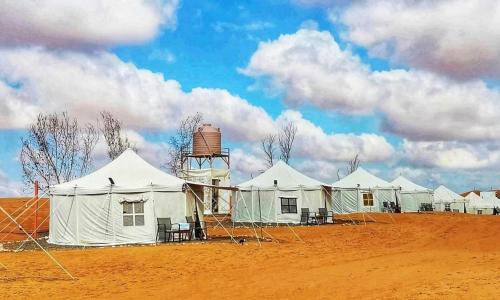 ShāhiqAlsarmadi Desert Camp的沙漠中一排白色帐篷,有水塔