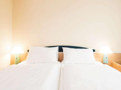 帕德博恩帕德伯恩宜必思酒店的配有白色床单和灯具的客房内的两张床