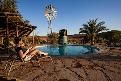 KarasburgCanyon Roadhouse Campsite的坐在游泳池旁带风车的椅子上的女人