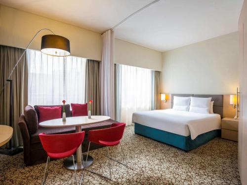 迪拜Novotel Suites Mall Avenue Dubai的酒店客房带一张床、一张桌子和椅子