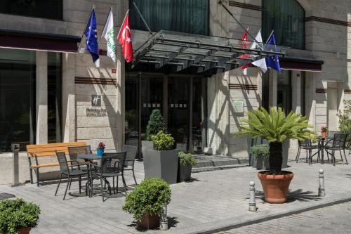 伊斯坦布尔伊斯坦布尔老城假日酒店的大楼前方带桌椅和旗帜的天井