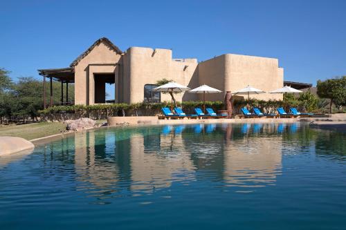 达沙萨巴尼亚岛奥沙希安纳塔拉别墅度假酒店的大楼前的带椅子和遮阳伞的游泳池