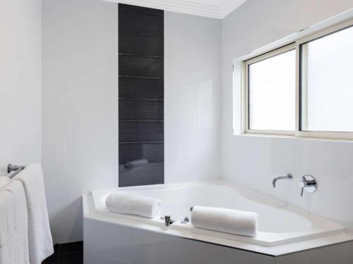 古尔本古尔本美居酒店的白色的浴室设有浴缸和窗户。