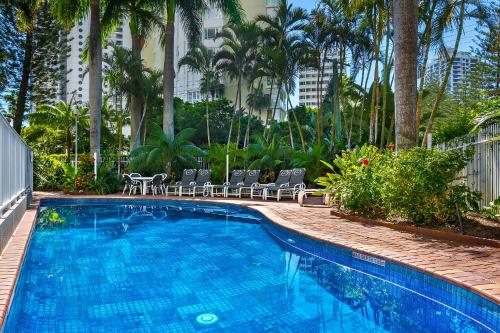 黄金海岸奥斯卡主海滩度假酒店的一个带椅子和树木的大型蓝色游泳池