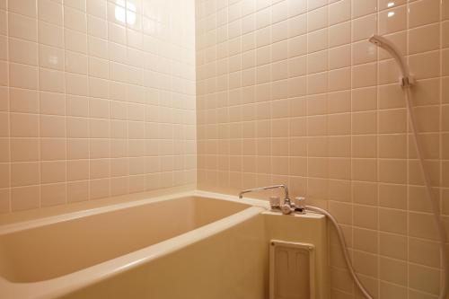 洲本市花历酒店的浴室铺有白色瓷砖,配有浴缸。