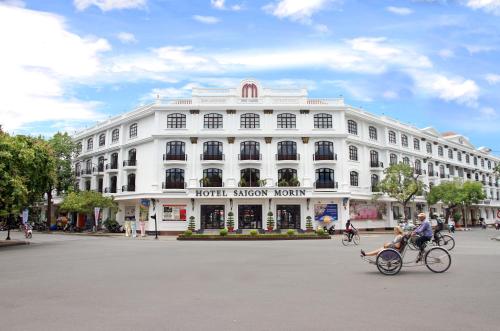 顺化西贡莫林酒店的骑着自行车在白色建筑前的人