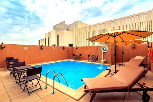 多哈Al Liwan Suites Rawdat Al Khail的一座带椅子和遮阳伞的大楼的顶部游泳池