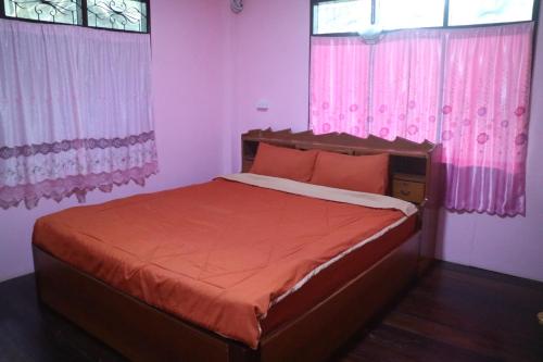 桑卡武里Baanmakpoo บ้านหมากพลู的一间卧室配有带橙色床单和粉红色窗帘的床