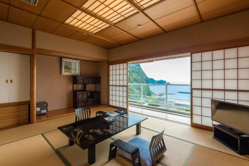 西伊豆町Nishiizu Crystal View Hotel的客厅设有桌子和大窗户
