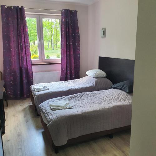 奥尔什丁JURAJSKI OLSZTYN的紫色窗帘和窗户的客房内的两张床
