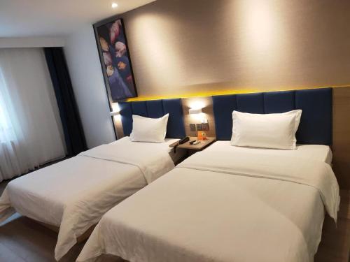 宜宾7天优品宜宾北门汽车站店的配有白色床单的酒店客房内的两张床