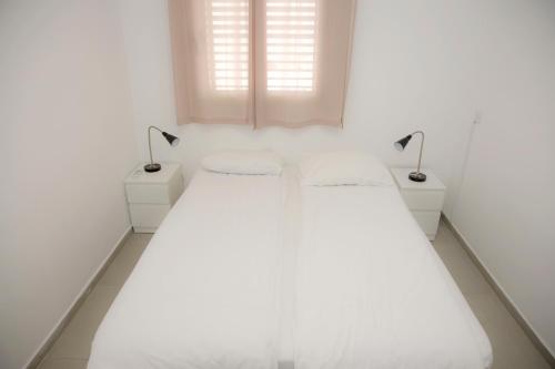 Beʼer OraPina BaMidbar的一间白色卧室,配有两张床和两盏灯。