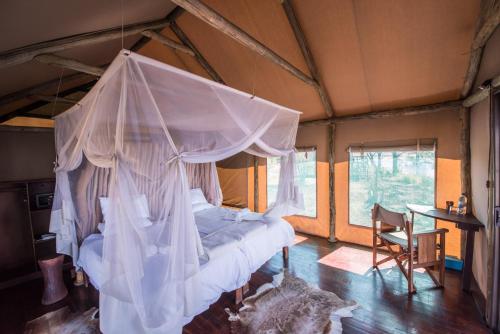 NgomaChobe River Camp的一间带一张天蓬床的卧室,位于带桌子的房间内