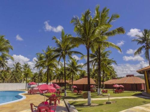 伊列乌斯Pousada E Restaurante Doce Desejo的一个带游泳池和桌子以及棕榈树的度假村