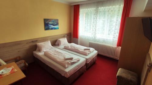 Morávka水坝酒店的一间卧室设有两张床,窗户配有红色窗帘